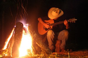 texan cowboy playing guitar in front of campfire